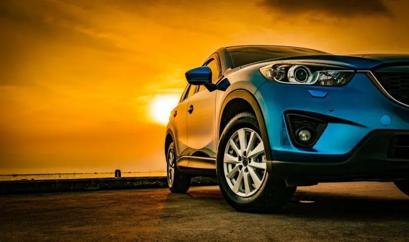 The Mufflerman, Mechanic Near Me A blue SUV is parked on a concrete surface, captured partially from the front-left angle. The vibrant orange and yellow sunset casts a warm glow across the scene, evoking thoughts of a trusted mechanic near me ready to ensure everything runs smoothly for sunset drives.
