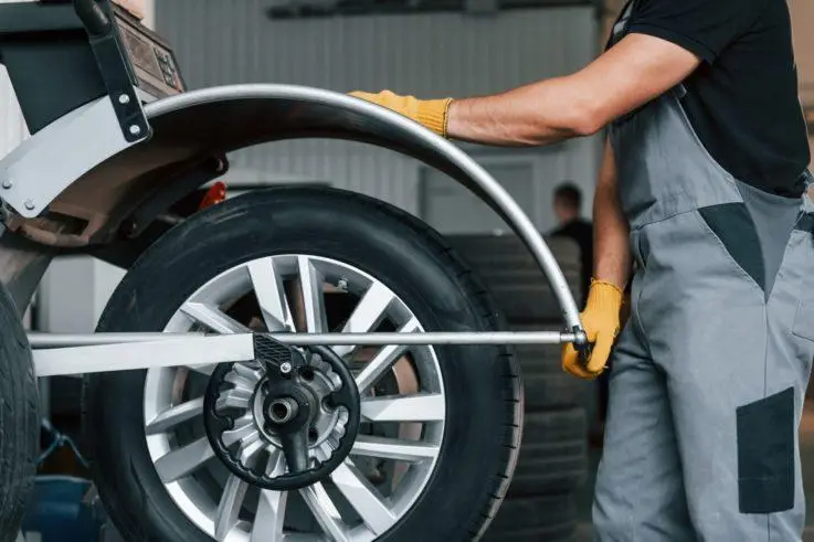 The Mufflerman, Mechanic Near Me In a local Tires Repair Shop Near Me, a mechanic in gloves and overalls fine-tunes a tire on a balancing machine. The tire rests on a sleek metallic stand, with attention drawn to the wheel and the skilled hands of The Mufflerman at work.